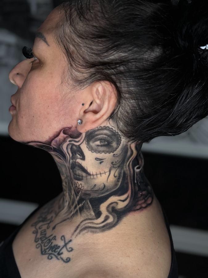 Catrina sugar-skull woman tattooed in black and grey realism down a neck and throat