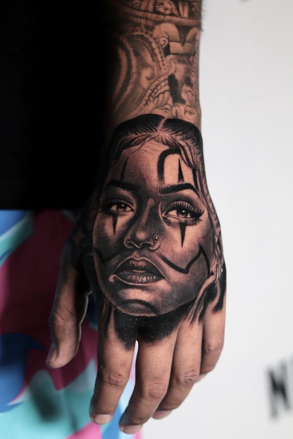 Chicana-style womans portrait tattooed in black and grey realism across the back of a hand
