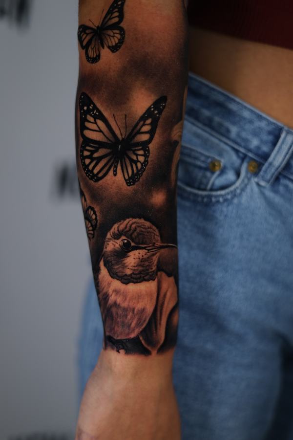Hummingbird and monarch butterflies in black and grey realism on a forearm