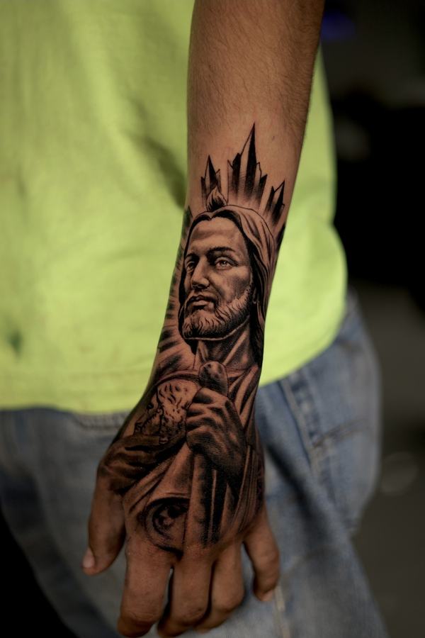 Robed figure of Jesus holding a staff, black and grey realism tattoo across a hand and wrist