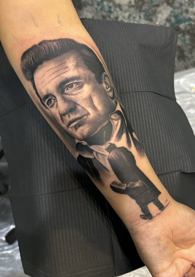 Realistic black and grey portrait tattoo of a man in a suit, tattooed down a forearm