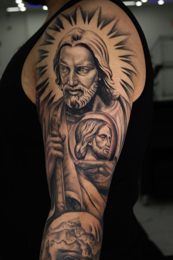 San Judas Tadeo portrait tattoo in black and grey realism across a shoulder and upper arm