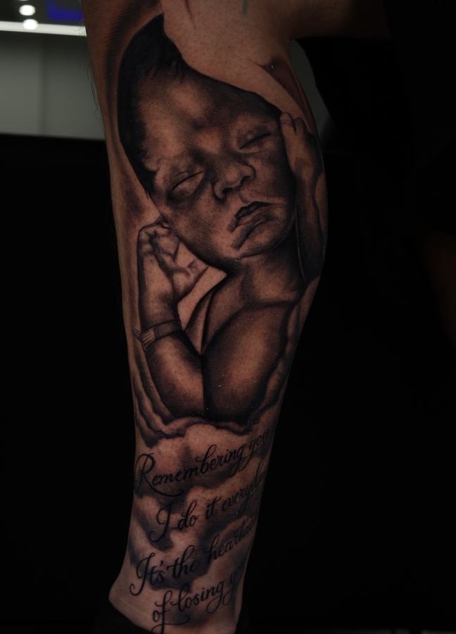 Sleeping newborn portrait with script lettering, black and grey realism memorial tattoo on a leg