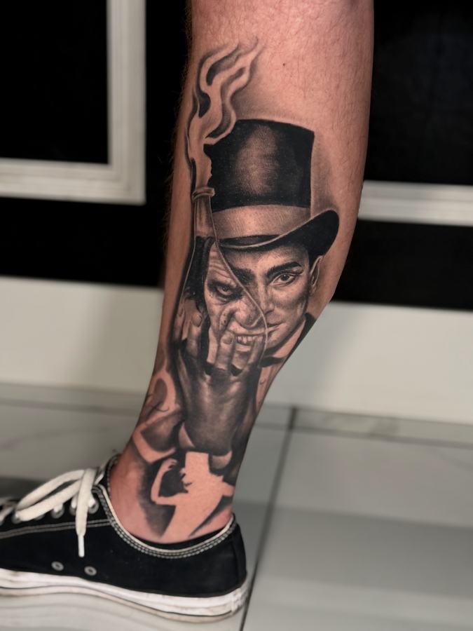 Portrait of a man in a top hat with a raised hand, black and grey realism tattoo on a lower leg