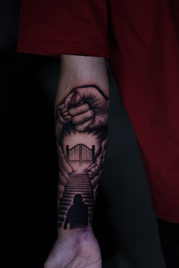 Feathered wing in black and grey, tattooed along a forearm