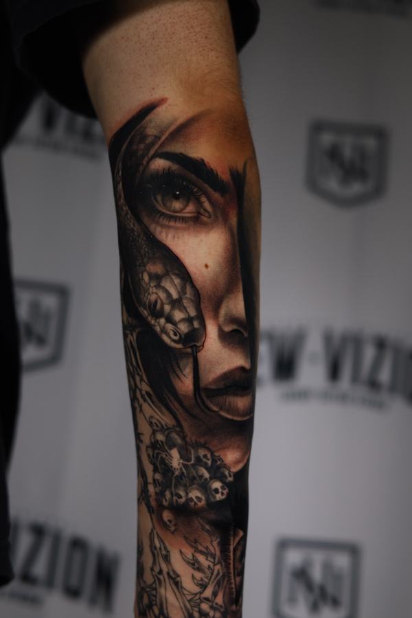 Womans face merging with a snake and skulls, black and grey realism tattoo on a forearm